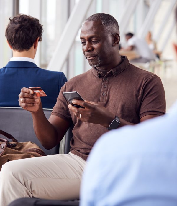 Businessman Sitting In Airport Departure Lounge Shopping Online Using Mobile Phone