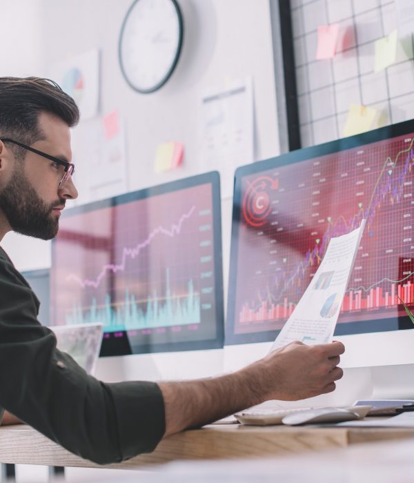 Side view of information security analyst looking at charts near graphs on computer monitors in